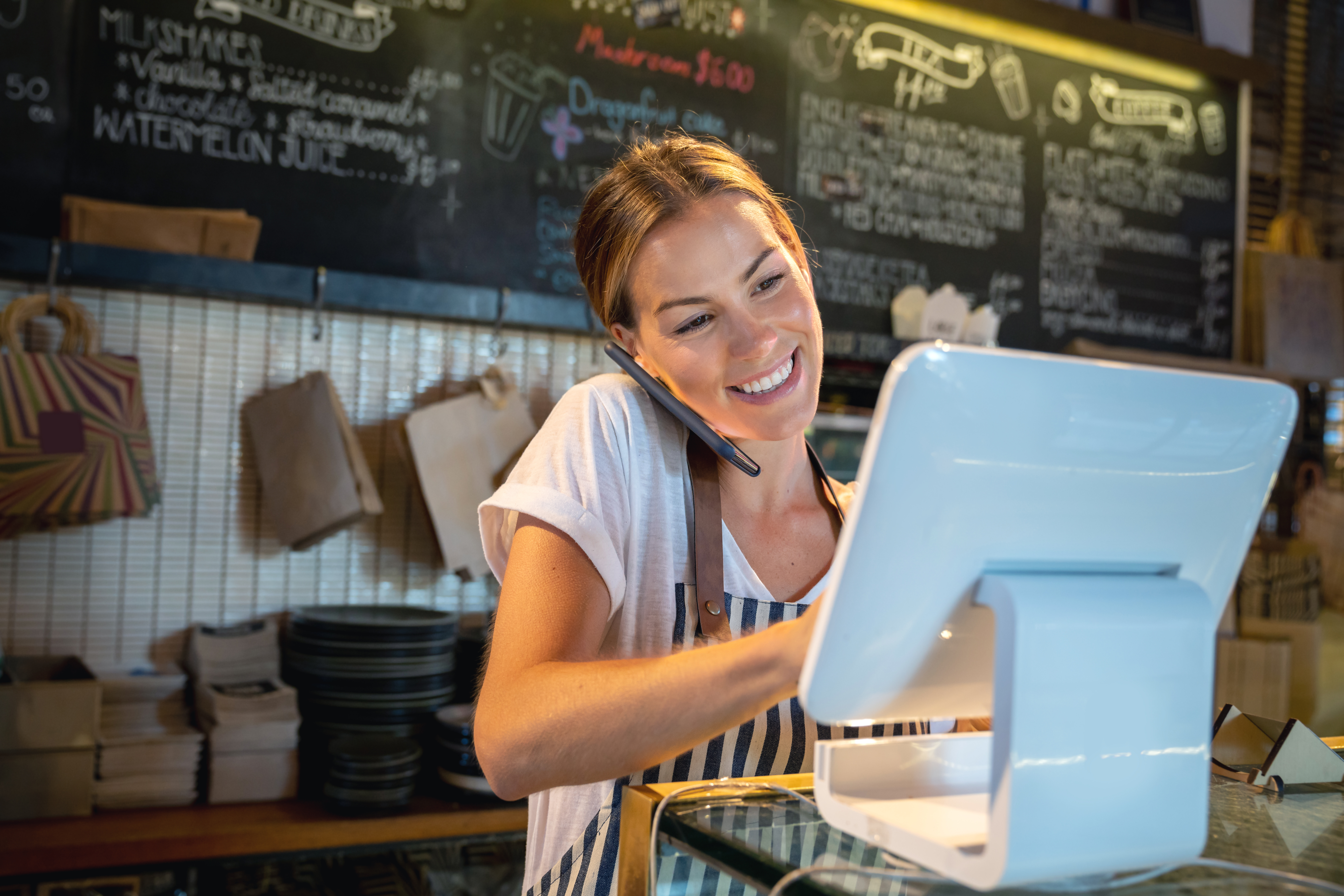 Woman talking on phone smiling while staring at a touch screen