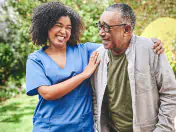 Nurse assists an elderly man walking through a garden.